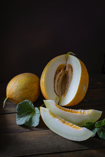 新鲜日本甜瓜整条切片，蜜瓜哈密瓜(Cucumis melo)叶木桌底。夏日水果养生理念。黑色食物背景静物，南瓜图片下载