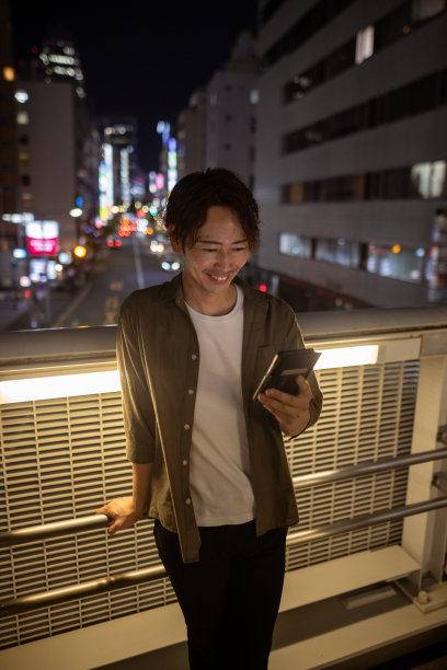 日本男人在夜晚的人行天桥上使用智能手机图片下载