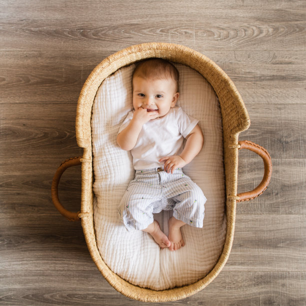 7个月大的男婴，有12个脚趾，穿着海岸服装，躺在一个舒适的海草摩西篮子里，白色亚麻布图片下载