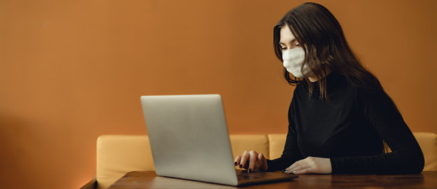 年轻女孩的肖像在黄色的背景与拷贝空间。医用口罩和笔记本电脑的概念。女性在电脑前工作图片下载
