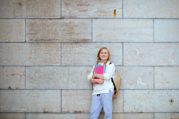 微笑的小学生穿着运动衫，在城市的户外靠墙图片下载