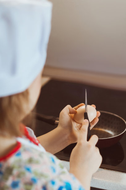 一个女厨师用刀把鸡蛋打到煎锅里。软焦点图片下载