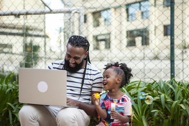 父亲在用笔记本电脑工作，女儿在玩图片下载