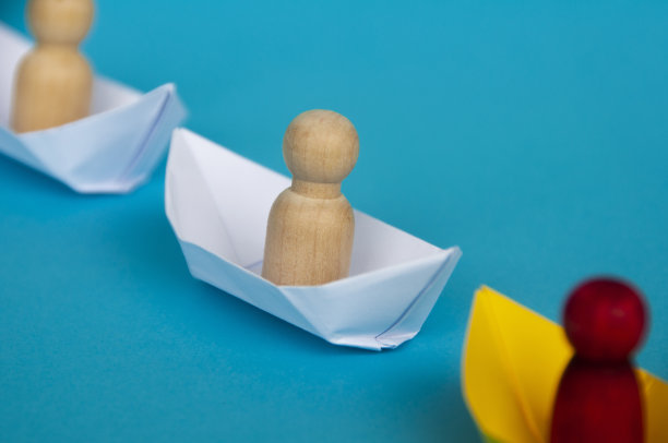 木制的娃娃人的形象在白色的纸船上折纸，跟随红色的娃娃在黄色的船上。复制空间和领导理念图片下载