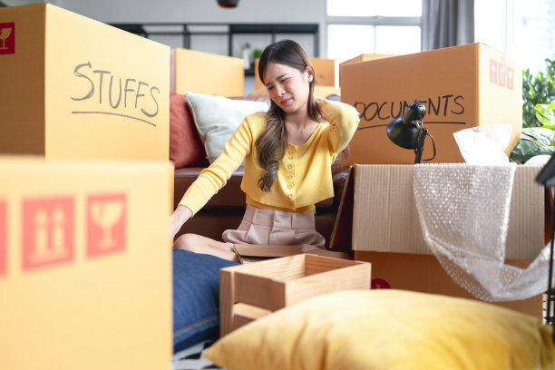 搬家对我来说是如此的无聊和辛苦，亚洲女头疼办公室的女肩膀疼，同时打包越来越多的东西，为搬家搬家的想法概念图片下载