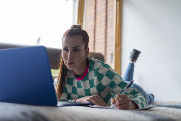 美丽的拉丁女人躺在床上做作业同时在线上虚拟课程图片下载