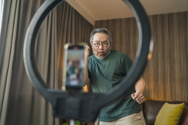 快乐的男性视频记录舞蹈在社交媒体上播出，男人在家里的客厅跳舞，有趣的庆祝有趣的病毒舞蹈自由周末。一名亚洲男子试图在智能手机上为视频直播练习舞蹈图片下载