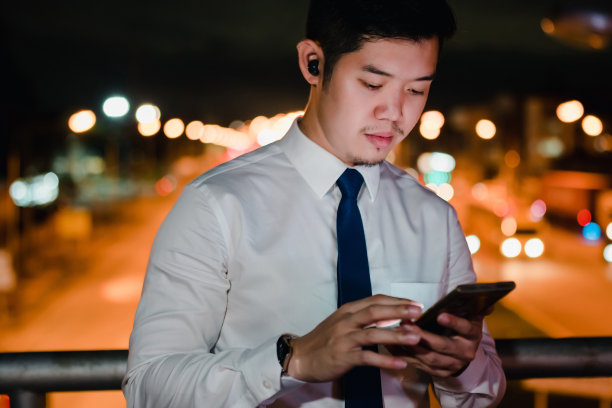 亚洲商人晚上在现代城市里用无线耳机听音乐图片下载