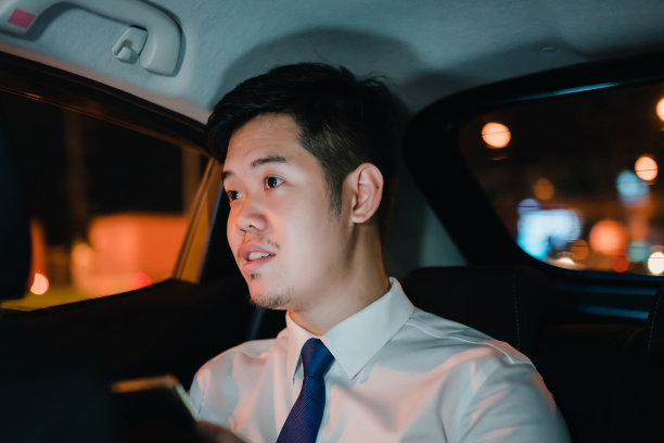 亚洲商人深夜坐在车后座用智能手机工作，晚上在车里看着窗外图片下载