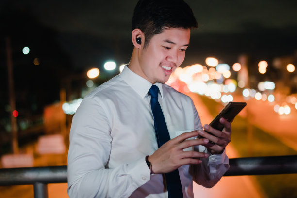 亚洲商人晚上在现代城市里用无线耳机听音乐图片下载