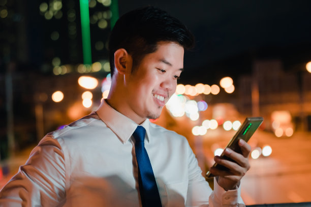 亚洲商人下班后用手机、智能手机走在城市街道上，晚上在城市里等车图片下载