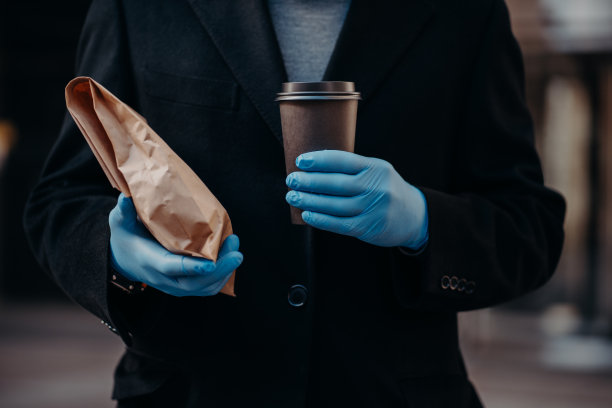 冠状病毒和隔离期间的配送服务。没有面孔的商人拿着外卖食品和一次性咖啡杯，为了安全戴着医用橡胶手套。大流行期间的营养。图片下载