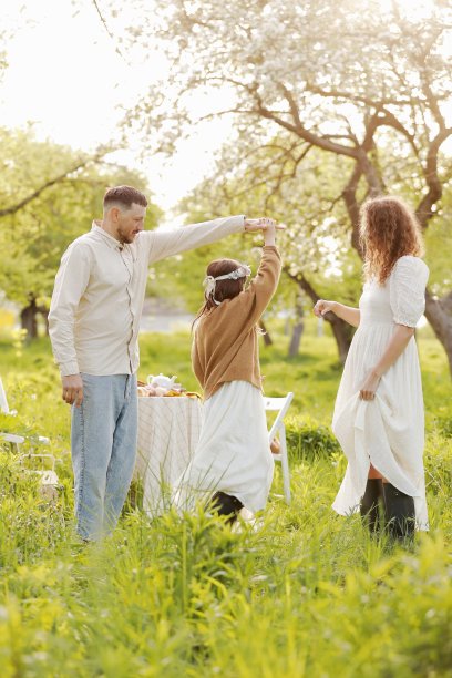 阖家欢度假期。妈妈，爸爸和小女孩放松和享受晚餐聚会一起在绿色的公园在夏天的夕阳。母亲节，父亲节和婴儿节。图片下载