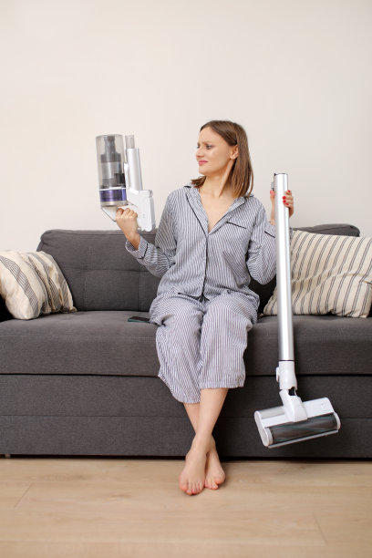 年轻女子带着可充电吸尘器坐在沙发上和家里。女孩试着按照说明书折叠吸尘器图片下载