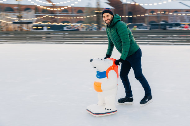 快乐男踩着冰鞋站在冰圈上，靠着特殊的辅助工具滑冰，有快乐，在镜头前摆出快乐的表情。没有经验的滑冰运动员练习滑冰。微笑的人有空闲时间享受爱好图片下载
