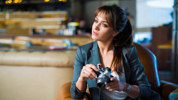 一位女记者坐在咖啡馆里，手里拿着相机。一个沉思的年轻女子手里拿着相机，目光移开了。图片下载