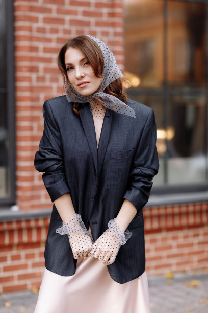 时尚年轻女性的肖像，发型，波尔卡圆点披肩和手套与化妆在外面摆姿势。一个穿着深色夹克的黑发女子出现在镜头前图片下载