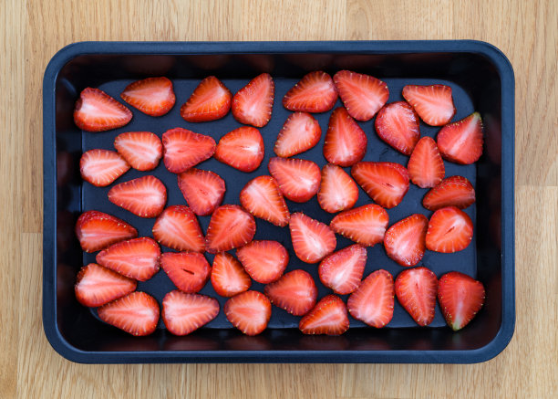草莓切成两半，放在木制背景的烤盘里图片下载