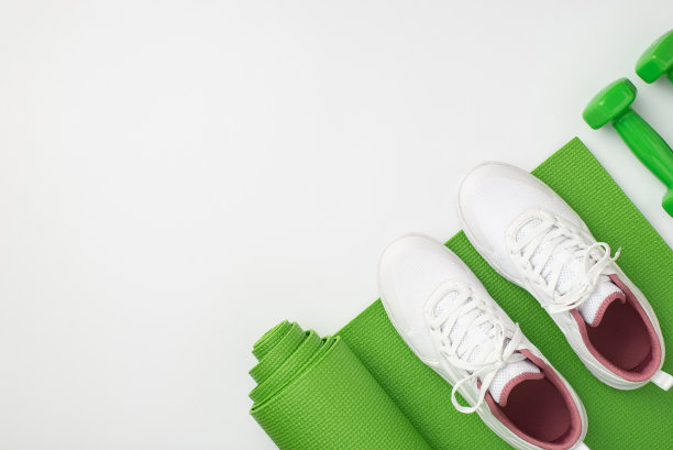 健身器材的概念。顶视图照片的白色运动鞋哑铃和绿色运动垫在孤立的白色背景与copyspace图片下载