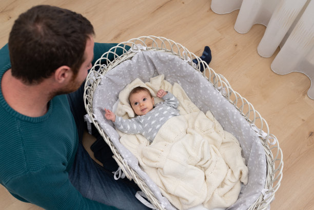 俯视图的父亲看着他3个月大的婴儿躺在一个可爱的柳条摇篮。图片下载