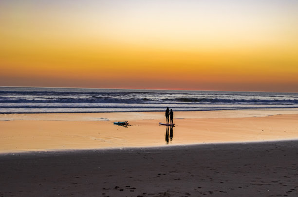 日落时分海滩上的冲浪者图片下载