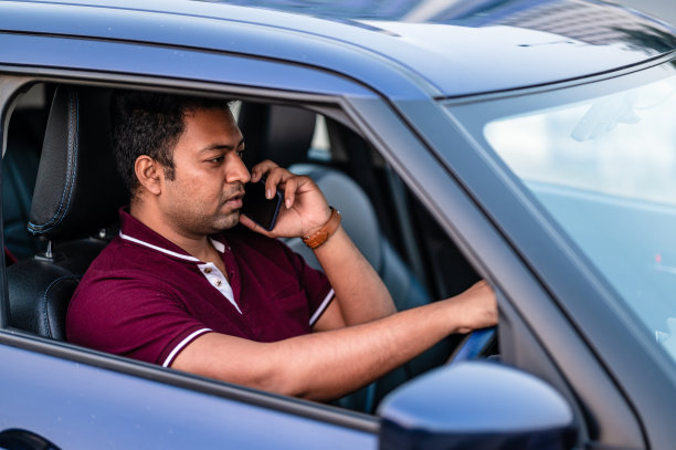一个年轻人在市中心的街道上一边开车一边用手机。图片下载