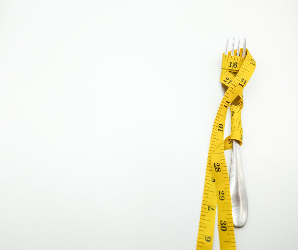 银叉上缠着黄色卷尺。白色的背景，概念，饮食控制，减肥，健康的生活方式图片下载