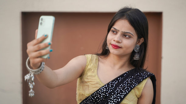 美丽的印度女孩在户外用她的手机自拍，穿着传统服装的开朗的亚洲女人点击自拍图片下载