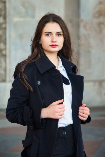 时尚的年轻漂亮时髦的女人在黑色黑色的秋天大衣在街上摆姿势。秋季流行趋势为微笑、快乐、有目的的女性。概念风格，美和成就目标。本空间图片下载