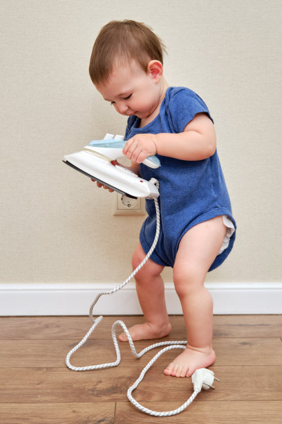蹒跚学步的宝宝在插座上玩热熨斗。一个手里拿着危险铁器的小男孩。一岁的孩子图片下载