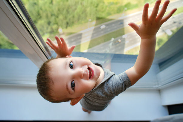 蹒跚学步的婴儿正站在窗台上的窗边。孩子在窗户边，手在玻璃上。一岁的孩子图片下载