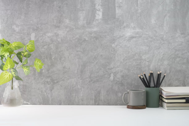 时尚的工作场所，咖啡杯，书，笔筒和盆栽植物在白色的桌子上靠阁楼墙。为你的文本复制空间。图片下载