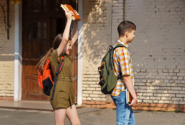 小学生们在学校操场上玩得很开心——一个十几岁的女孩想用书本打一个男孩的头图片下载