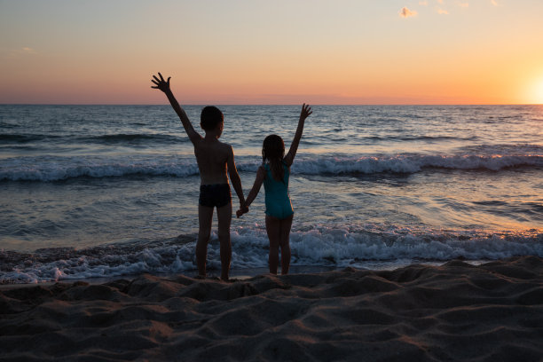 一个小男孩和一个小女孩的剪影手牵手在海边日落图片下载