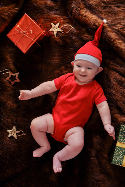 婴儿婴儿的男孩戴着圣诞老人的帽子，棕色毛皮大衣和礼物的盒子。一岁半的孩子，过年平躺俯视图图片下载