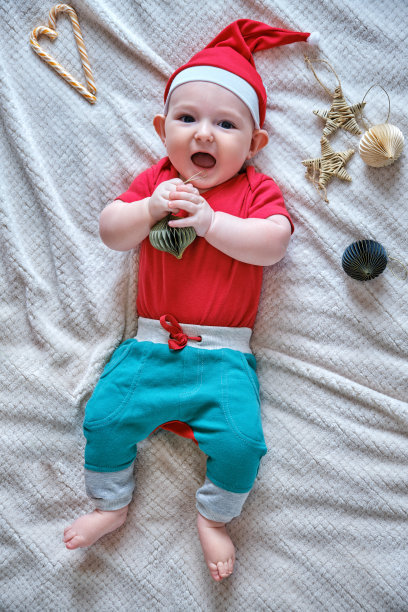小男孩戴着圣诞帽，白色毯子上有圣诞装饰。一岁半的孩子，过年平躺俯视图图片下载