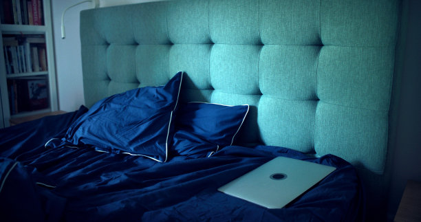 空荡荡的卧室里凌乱的床单。笔记本电脑落在后面。图片下载