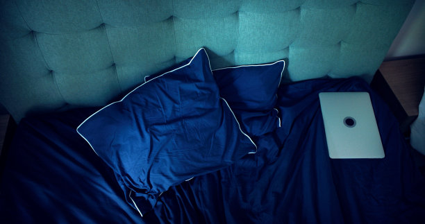 空荡荡的卧室里凌乱的床单。笔记本电脑落在后面。图片下载