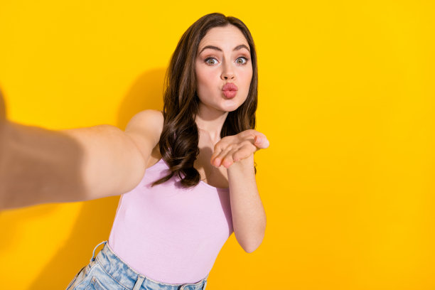可爱漂亮女孩的照片自拍手臂手掌送飞吻你孤立在黄色的背景图片下载