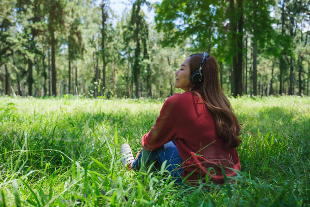 一个美丽的年轻亚洲女人的肖像享受听音乐与耳机坐在公园图片下载
