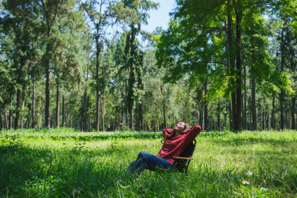 一个美丽的年轻女子的肖像形象，双手放在脑后，坐在公园的椅子上放松图片下载
