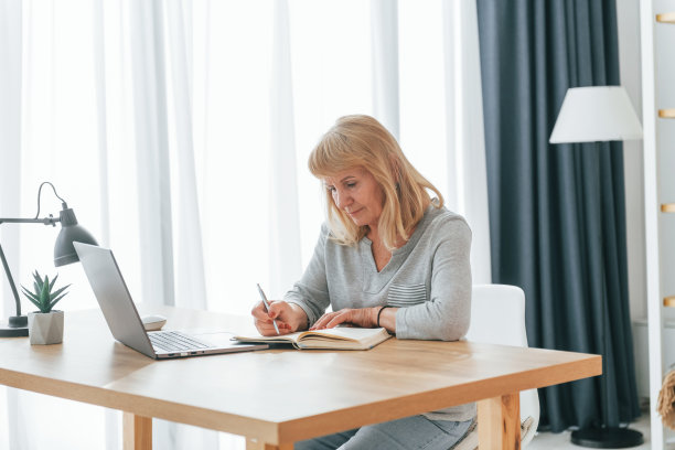 带着笔记本电脑坐在桌边。一位红头发的老妇人独自在家图片下载