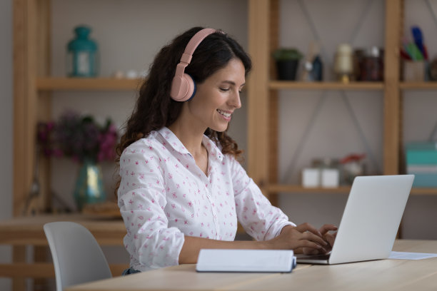 西班牙裔女性坐在办公桌前，戴着耳机，用笔记本电脑工作图片下载