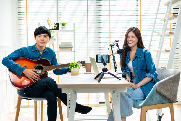 年轻夫妇戴着耳机在社交媒体的个人音乐频道上实时唱歌、弹吉他。一对迷人的夫妇坐在沙发上，拿着吉他。图片下载