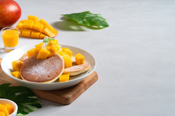 美味的日本蛋奶酥煎饼，芒果丁和果酱在白色的桌子背景。图片下载