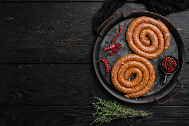 生肉香肠，在黑色的木制桌子背景上，俯视图平铺，有文字的复制空间图片下载