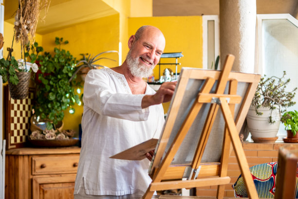 一个自信快乐的老人享受着他的空闲时间和生活，在他的客厅里画画。图片下载