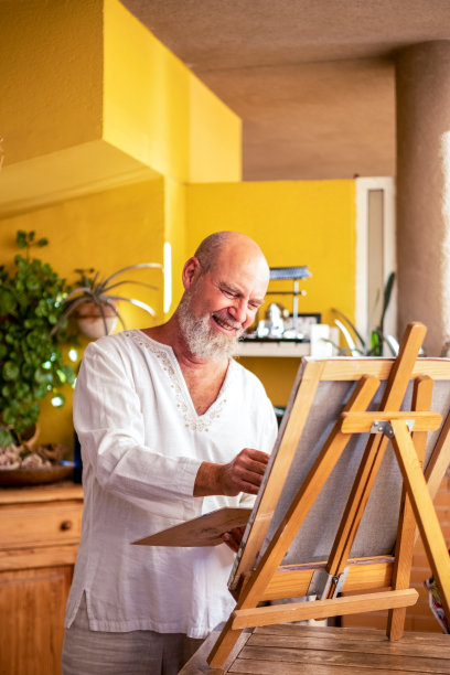 一个自信快乐的老人享受着他的空闲时间和生活，在他的客厅里画画。图片下载