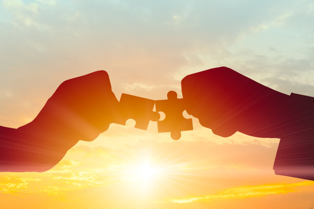 业务团队合作，加入伙伴合作理念。在清晨的天空上，两只手把两块拼图连在一起的剪影。图片下载