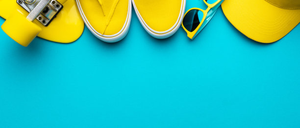 黄色棒球帽，太阳镜，运动鞋，迷你巡洋舰板在蓝色的背景图片下载
